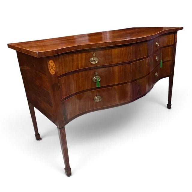 An exceptional and highly sophisticated English George III Hepplewhite serpentine sideboard, handcrafted circa 1790–1805...
