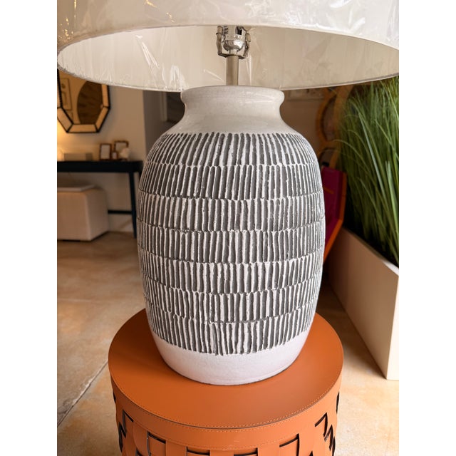 This contemporary table lamp features a textured ceramic base in soft white and charcoal gray, creating a striking yet...