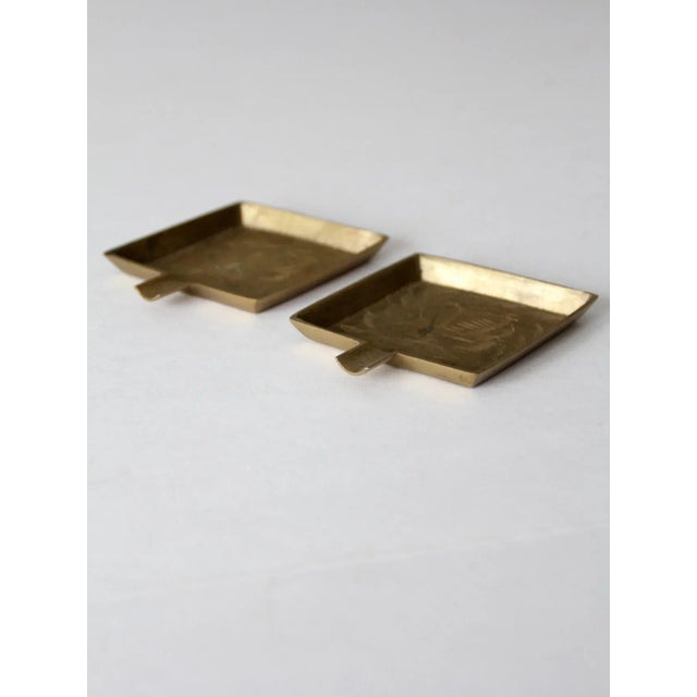 This is a pair of vintage brass ashtrays. The rectangular dishes feature a floral design with a single hold.