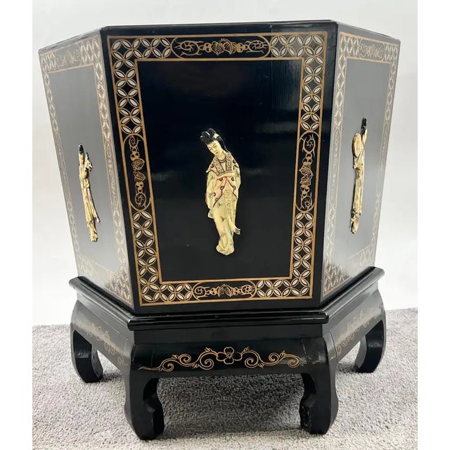 A striking Asian black lacquer hexagonal side table featuring hand-painted gold and white decorative borders framing...
