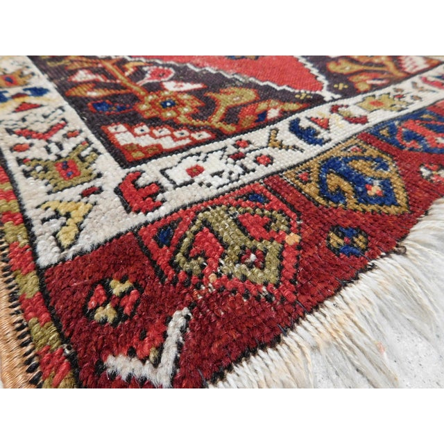 Oversized geometric medallion on rich in tone red field, within floral decorated spandrels. Ivory border with nomadic...