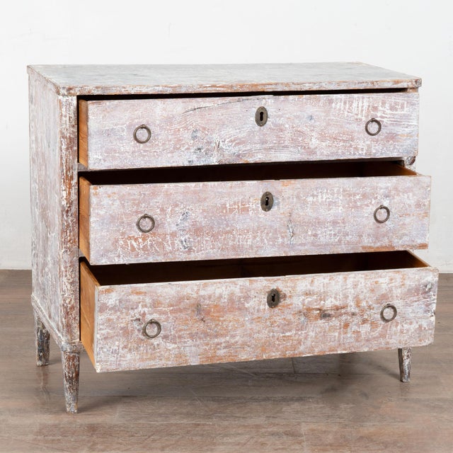 19th century Swedish chest of three drawers crafted in pine. The painted surface has been scraped, revealing layers of...