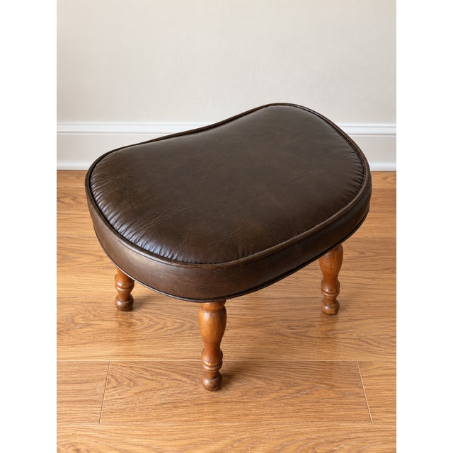 Mid-century modern kidney-shaped footstool featuring a rich brown leather cushion with beautiful patina and turned wooden...