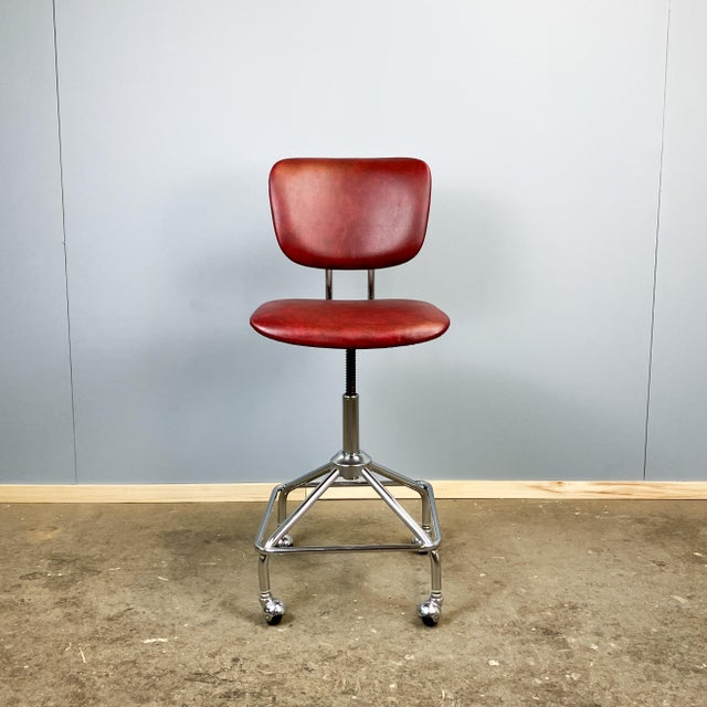 Iconic swivel chair with a uniquely shaped chrome frame, the typical encapsulated casters, and a marbled, burgundy faux...