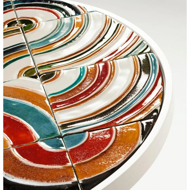 This piece comes in multiple configurations and finishes. Pictured with a circled multicolored ceramic tiled top, a wooden...