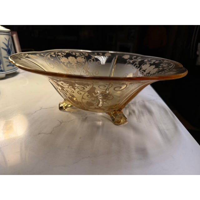 This is an amber-yellow vintage glass footed bowl with an etched floral and scrolling vine design, likely a Fostoria...