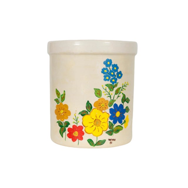 A hand-painted stoneware utensil holder jar. The front side is decorated with simple flowers in primary colors over a...