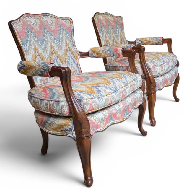 Pair of French Louis XV style bergère fauteuils featuring carved walnut frames with graceful cabriole legs, shaped aprons,...