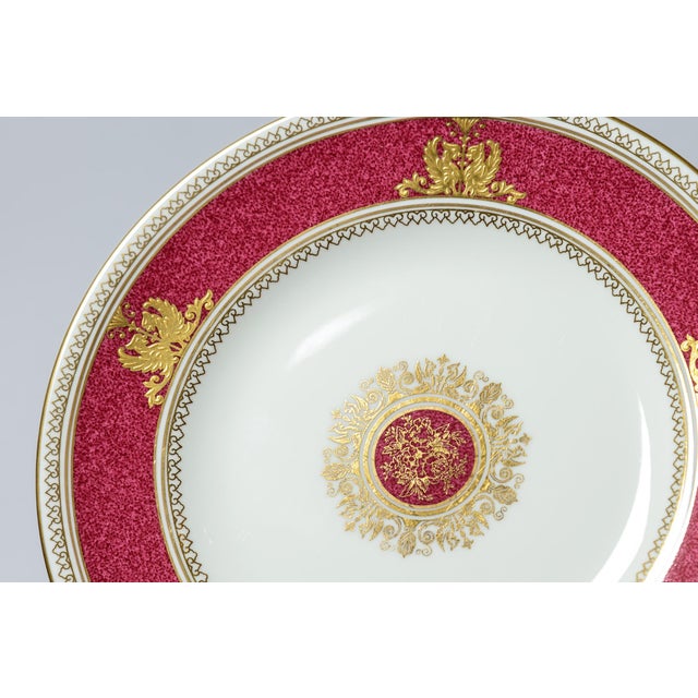 A pretty set of 16 plates with a ruby powder finished collar accented with a raised double griffin gilt motif and central...