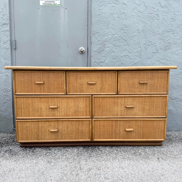 A warm and textural vintage dresser featuring a natural rattan frame with woven wicker drawer fronts and coordinating...