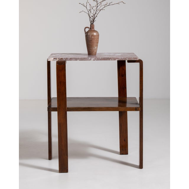 A compact Art Deco side table featuring a marble top and clean geometric lines. The contrast between materials creates a...