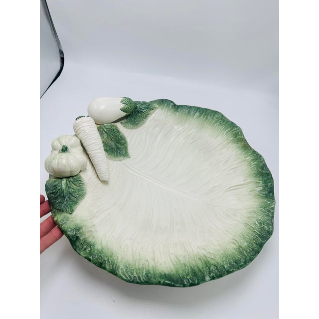 This is a beautifully crafted ceramic serving bowl, designed to resemble a large cabbage or lettuce leaf. The bowl has a...