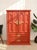 A bold and beautifully detailed vintage armoire featuring a rich, deep red painted finish and ornate gold-tone hardware....