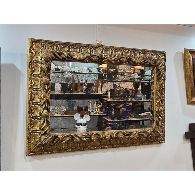 An exceptional 18th-century French mirror featuring a substantial carved and gilded wooden frame of remarkable decorative...