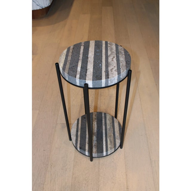 Two rounds of black and gray travertine rest in between five legs of black steel. Dimensions: 14" W X 24" H X 14" D...