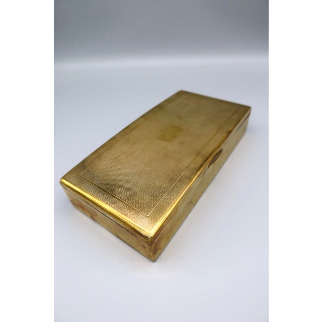 Rectangular English brass box with hinged lid and wooden interior, marked “Made in England” on the base. The lid features...