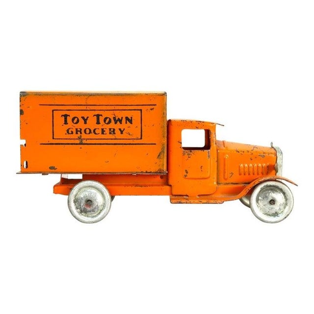 An antique pressed steel advertising truck, dating to approximately 1920. This toy vehicle features an orange painted...