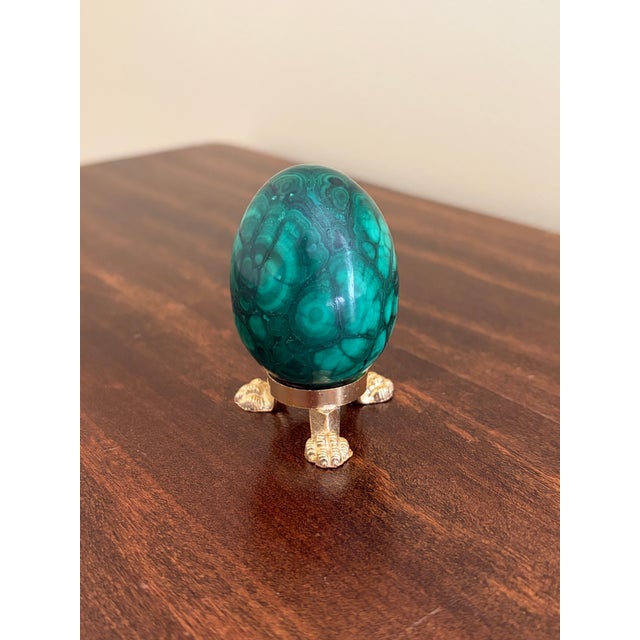 A beautifully proportioned malachite egg in richly veined shades of green and black resting on a neoclassical style brass...
