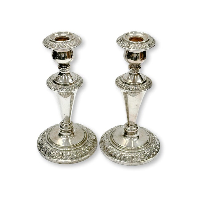 Early 20th century English silverplate candlesticks offered as a pair. The elegant tapered stems rise from broad decorated...