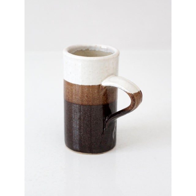 A vintage handmade studio pottery mug with a tall, slender form and a subtle vertical profile. finished in layered glaze...