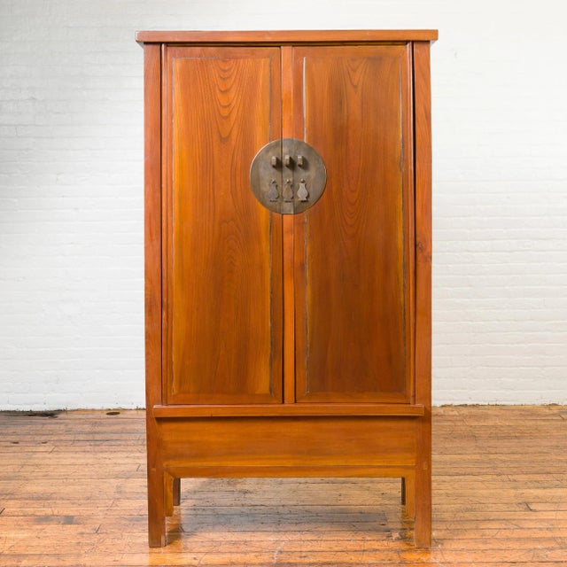 A Chinese Qing Dynasty elmwood cabinet from the 19th century, with bronze medallion hardware and inner drawers. Crafted in...