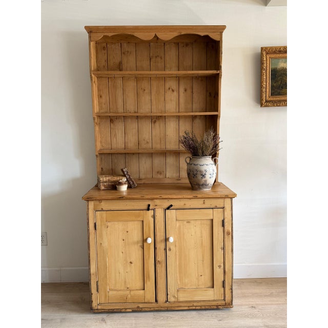 An English pine stepback hutch with an open plate rack above, the top edged by a scalloped apron, over a base of twin...