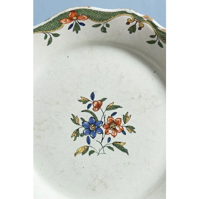 An 18th-century French faience plate from Rouen, decorated with a stem of flowers and leaves in the centre in red, green,...