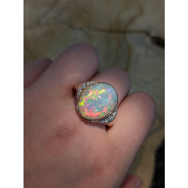 This captivating ring features a luminous 7.11ct oval Ethiopian opal (16.8x13.2mm), celebrated for its vivid play of...