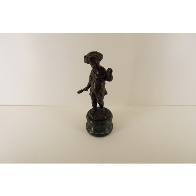 This vintage bronze figurine depicts a young boy in a classical toga, rendered with charming detail and a soft sense of...