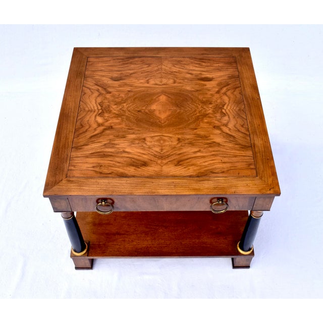 A two tier book- matched flame grain Walnut side table with one drawer showcasing Neoclassical design elements in the...