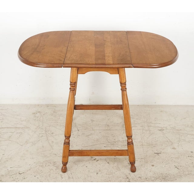 Vintage Traditional style end table in medium tone wood, with a drop leaf top and turned legs with low stretchers. There...