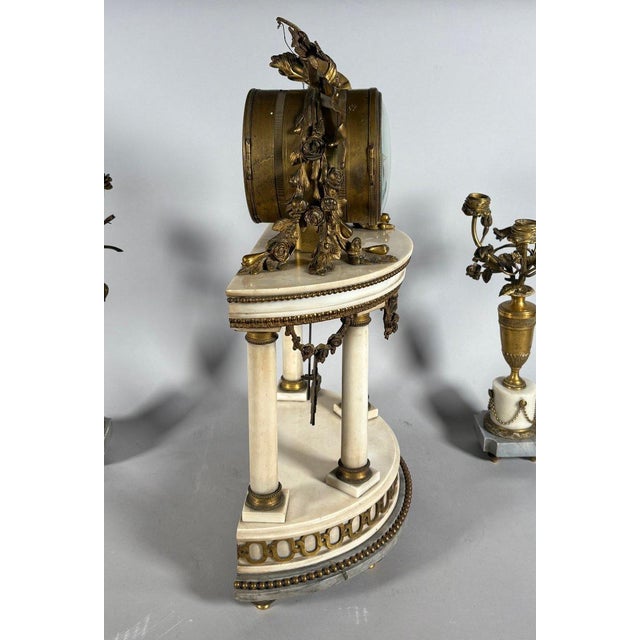 A Louis XVI style mantel clock and floral candelabra set. The mantel clock features four white marble columns on a blue...
