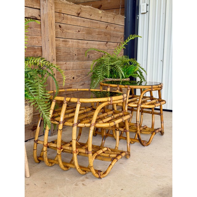 A fabulous pair of true vintage bent rattan side tables featuring sculptural curved frames, woven lower shelves, and their...