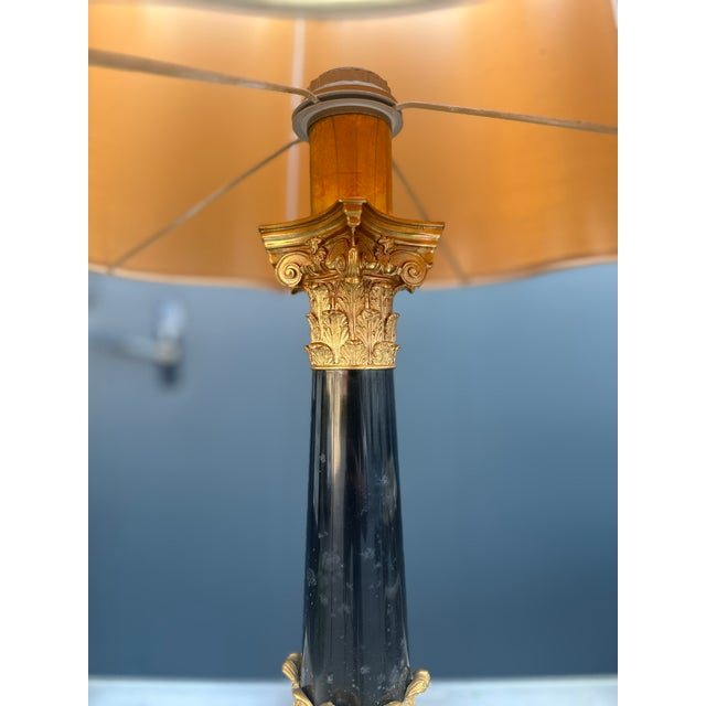 Empire-style table lamp featuring a black marble column base and finely chiseled gilded bronze details. The upper part of...