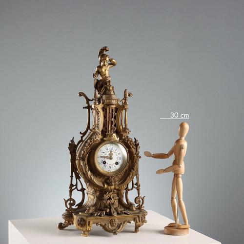 Bronze mantel clock in the shape of a lyre surmounted by a figure of Cupid wearing a plumed helmet. Note the rich and...