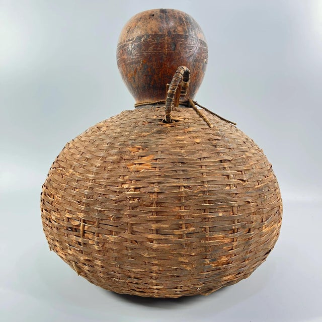 Handcrafted natural calabash encased in woven fiber for protection and transport. Features original binding and side loop...