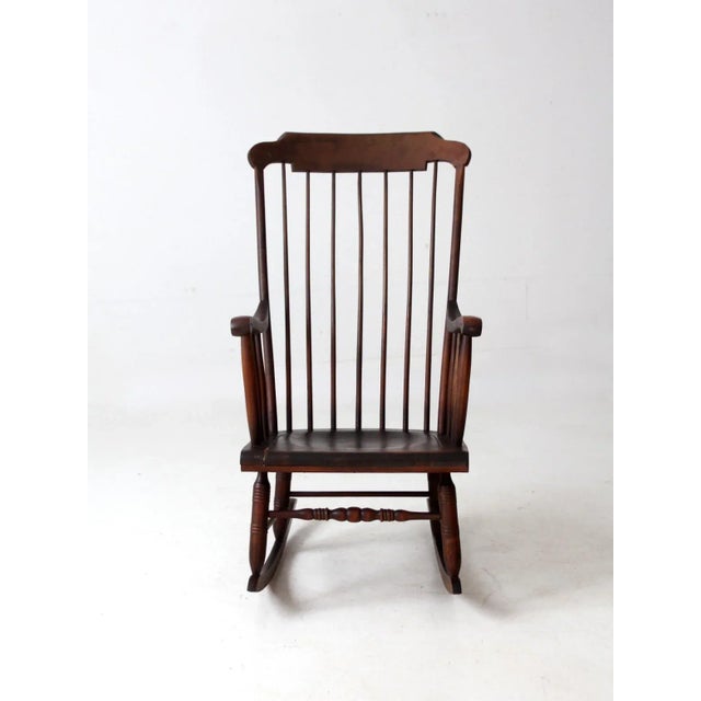 An antique American Windsor rocking chair distinguished by slender spindles, elegantly shaped arms, and a balanced,...