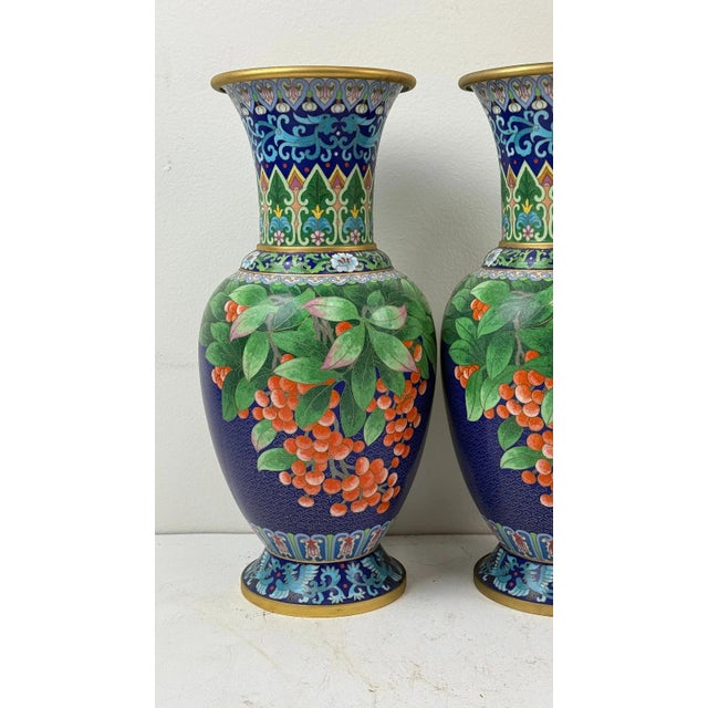 Pair of Chinese cloisonne vases featuring blue ground with orange berry branches and foliage, detailed enamel work, likely...