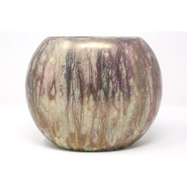 A 1961 ceramic vase, with an oval, rounded form. It is hand-decorated with purple and metallic gold flowers, over a mint...