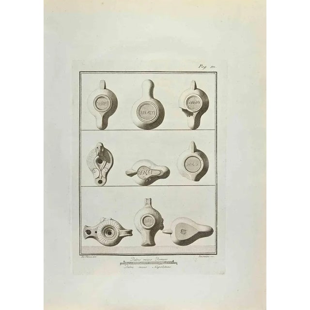Oil Lamp from "Antiquities of Herculaneum" is an etching on paper realized by Iacomino e Nicola Vanni in the 18th Century....