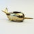A vintage brass votive candle holder in the shape of a narwhal. The body of the narwhal is a more muted colored gold while...