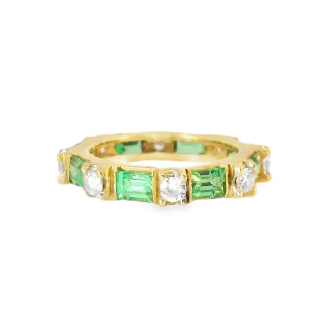 Estate 14K yellow gold eternity band featuring alternating baguette-cut emeralds and round diamonds, a timeless symbol of...