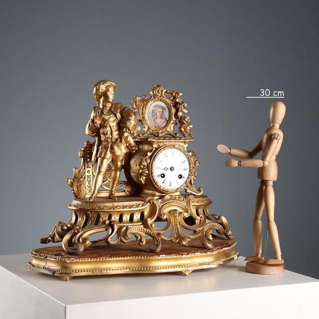 Gilded antimony clock with a wide base decorated with leafy scrolls. Enamelled metal dial with Roman numerals surmounted...