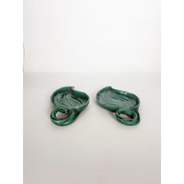 An elegant pair of glazed ceramic dishes, crafted in a stylized leaf shape with an integrated scroll handle. Their deep...