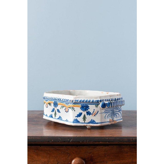 An 18th-century French faience jardinière from La Rochelle, with an octagonal basin raised on feet and flanked by two...