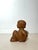 Expressive carved wooden sculpture depicting a seated child, executed with a sober yet deeply emotional presence. The...