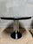 A striking postmodern side table featuring a sculptural chrome column base and a black round tabletop. Its bold geometric...