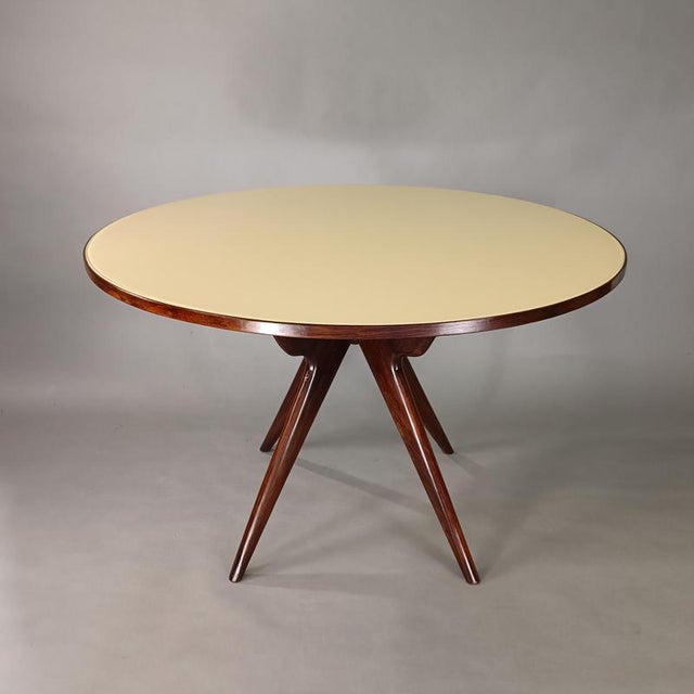 Elegant Italian-designed round table in the style of Osvaldo Borsani, 1950s. Crossed compass legs in mahogany-colored...