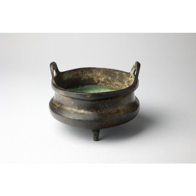 A solidly cast Chinese bronze tripod censer of compressed globular form, raised on three tapered feet and fitted with a...