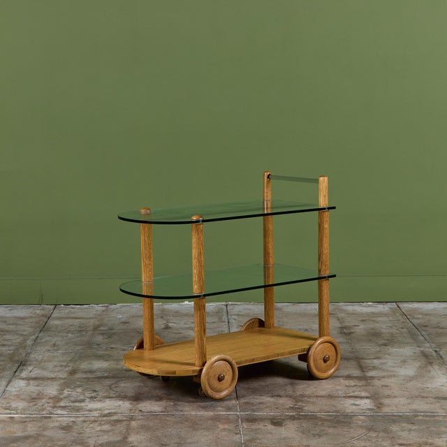 Gilbert Rohde maple bar cart, c.1940s, USA for Herman Miller. This playful piece features two glass shelves and one maple...